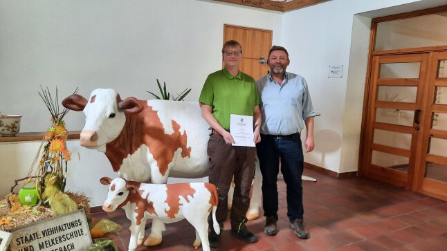 Jachim Meyer und Georg Hammerl schauen in die Kamera. Sie stehen neben einer Plastikkuh. Joachim hält eine Urkunde.