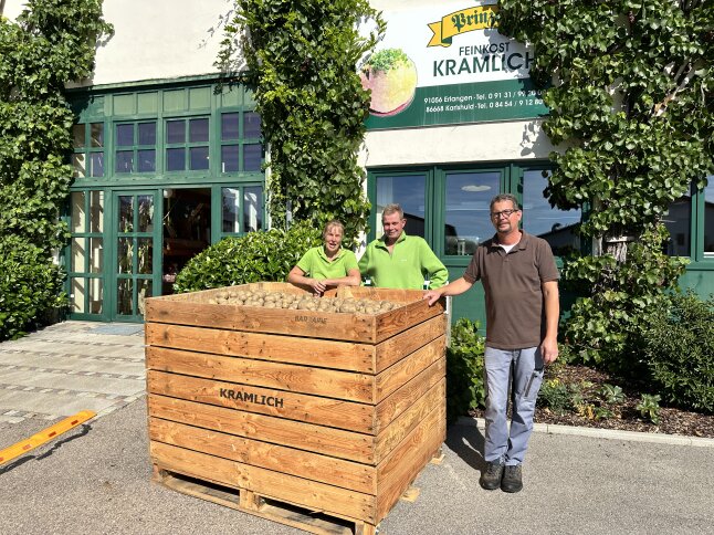 3 Personen stehen hinter bzw. vor einer großen Kartoffelkiste