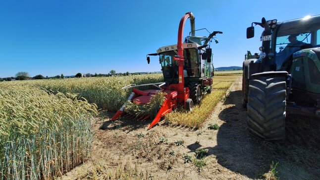 GPS Häcksler steht in einem gedroschenen Weizenfeld neben einem Traktor