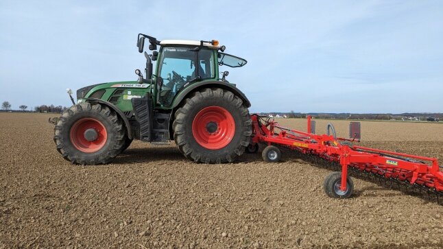 grüner Traktor mit roten Felgen und rotem Unkrautstriegel