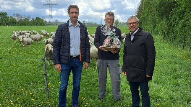 3 Männer stehen vor Schafen einer erhält ein Geschenk