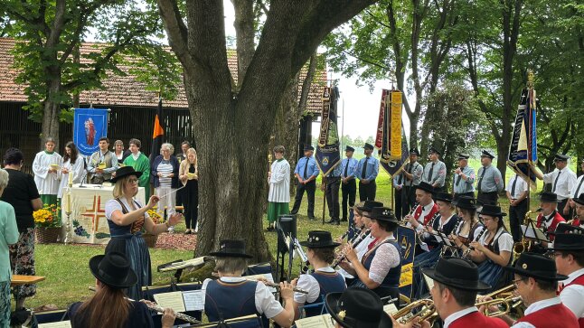 auf einer Wiese sind viele Leute mit Altar und Pfarrer sowie eine Musikkapelle