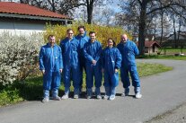 Sechs Personen in blauen Schutzanzügen stehen vor Stall