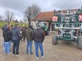 Ein Mann steht neben einem landwirtschaftlichen Gerät zur Gülleausbringung und erklärt hierzu den Studenten die Funktionsweise
