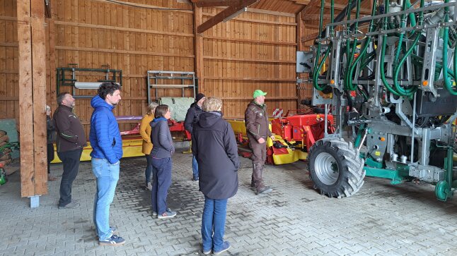 Mann in brauner Kleidung erklärt ein landwirtschaftliches Gerät zur Gülleausbringung